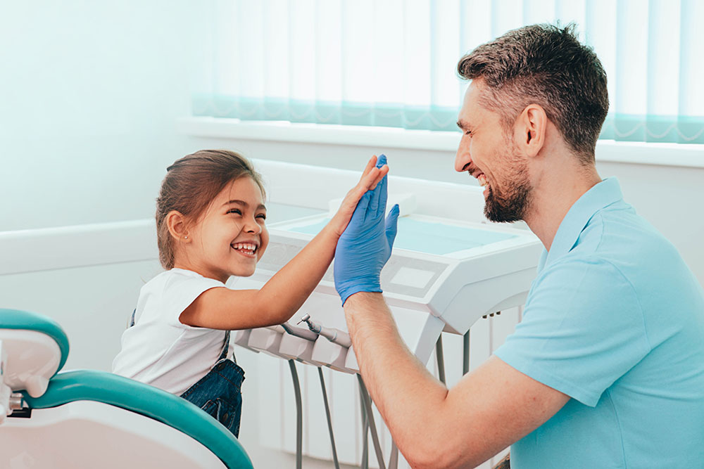 child at the dentist office giving dental assistant a high five