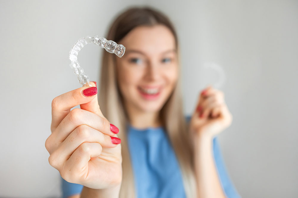 Female hand holding Invisalign, the invisible braces aligner at face