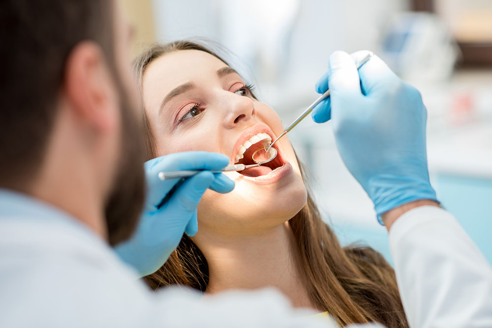 Dentist examining patient teeth with a mouth mirror and dental excavator.