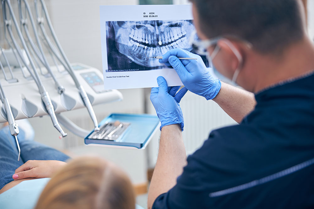 Male dentist is holding photo of woman teeth and explaining problems before starting treatment in office