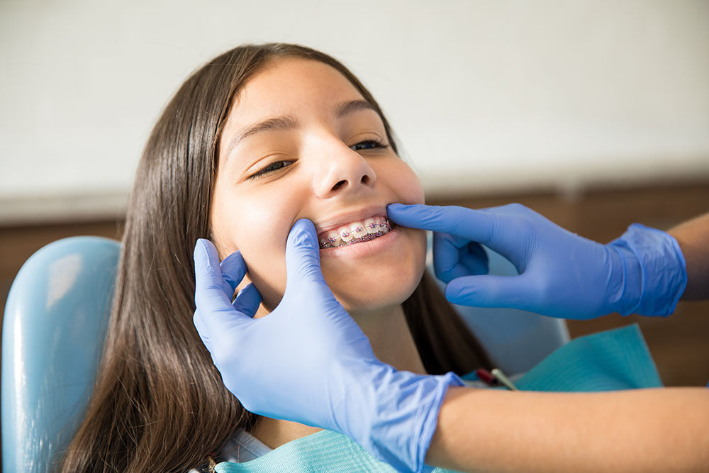 Teenage girl with braces being examined by dentist wearing gloves at clinic
