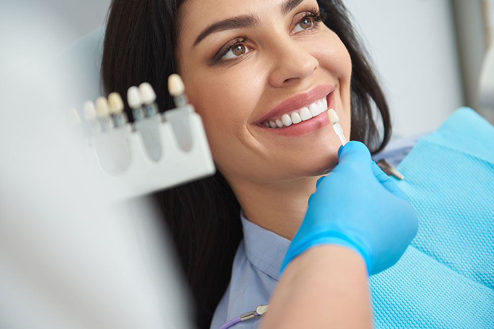 Close up of dentist holding dental crown near female mouth